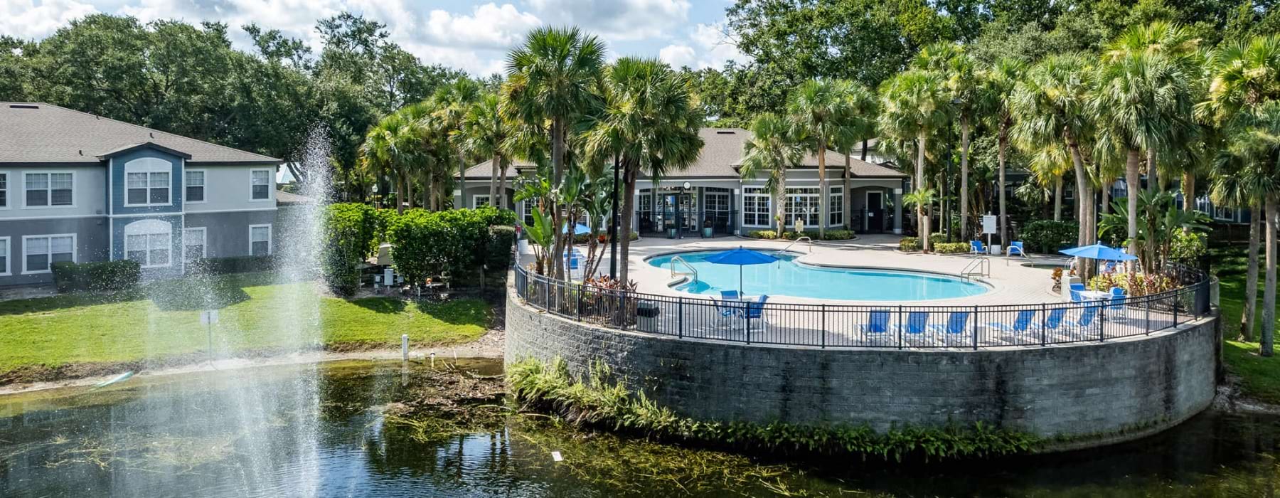 a fountain in a pond with a building and palm trees in the background